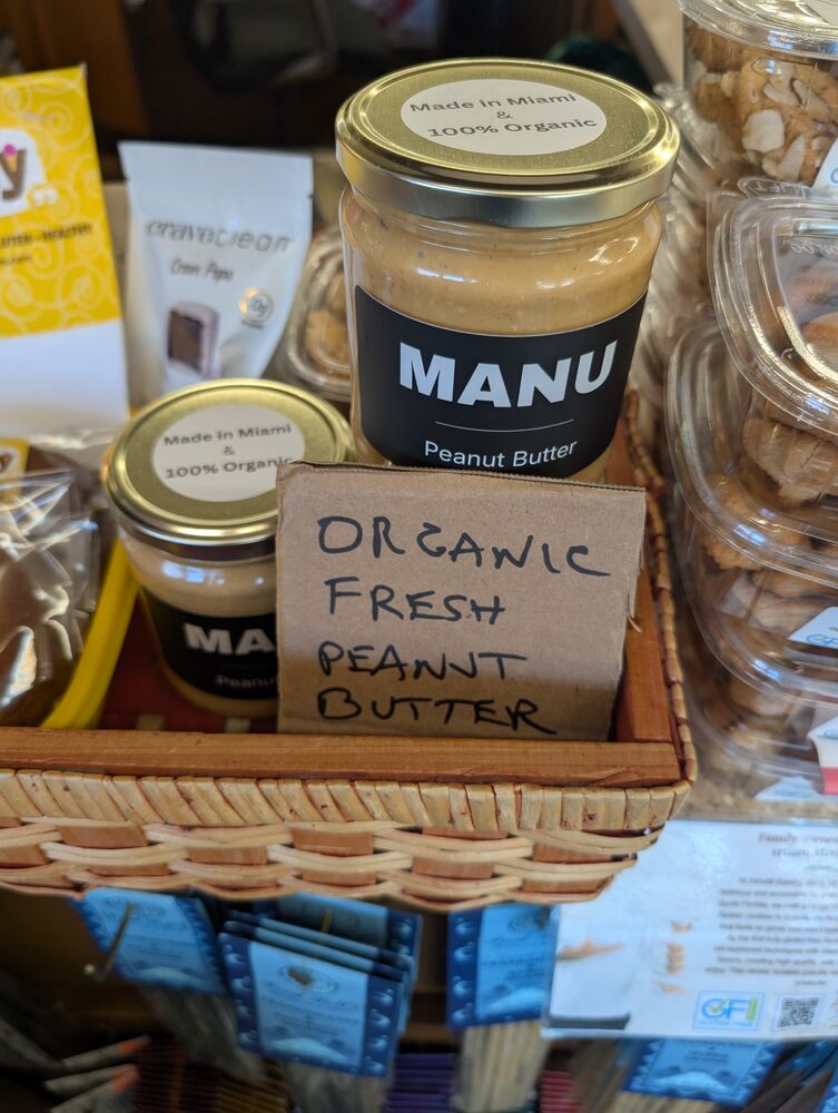 A MANU jar in a store basket next to a handwritten sign reading organic fresh peanut butter.